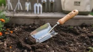 Close-up of a sturdy hand trowel from a beginner garden tool set digging rich organic garden soil in a Canadian backyard.